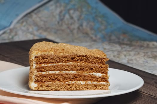Piece of honey cake on plate near map on the table.
