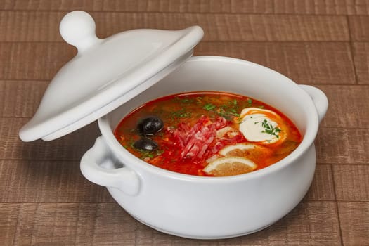 Solyanka - Russian traditional meat soup. Russian soup saltwort in round plate on wooden background.