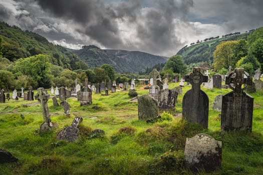 Wicklow, Ireland, August 2019 Ancient graves with Celtic crosses in Glendalough Cemetery with mountains and dramatic storm sky in background