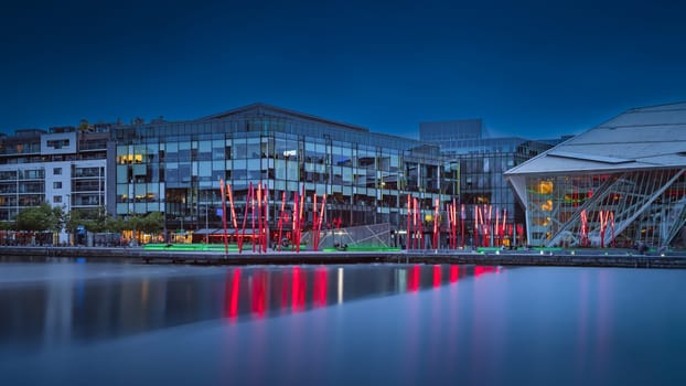 Dublin, Ireland, August 2019 Grand Canal Square in docklands with theatre, red sticks, shops and buildings at night or blue hour
