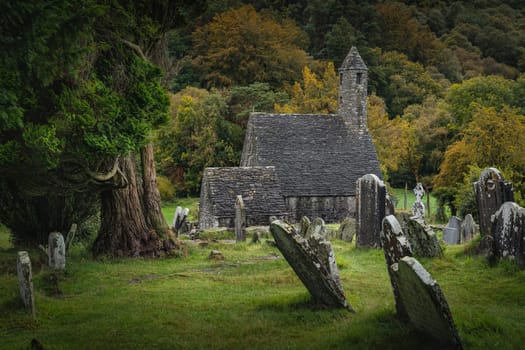 Medieval church, ancient graves, Celtic crosses in Glendalough Cemetery with autumn forest and mountains in the background, Wicklow, Ireland