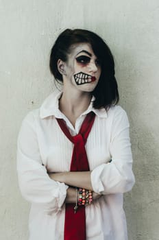 Scary woman with halloween makeup mask on her face in front of grunge wall.