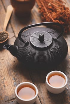 Still life with traditional asian herbal tea prepared in vintage cast iron teapot with organic dry herbs on rustic wooden table. Retro filter.