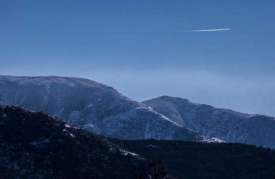Airliner flying over the snowy peaks of the Sierra de Gredos. La Garganta, Ambroz Valley, Extremadura, Caceres, Spain