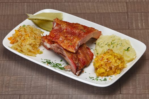 Plate with smoked ribs with mashed potato, pickled cucumber, cabbage on wooden table
