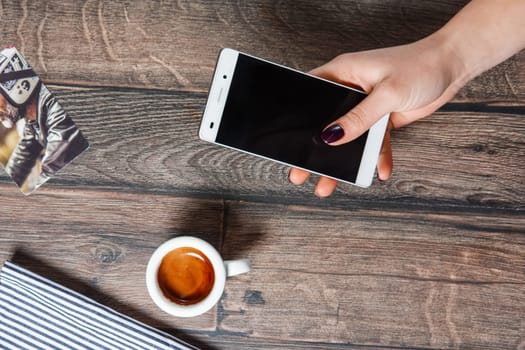 Top view of table with cup of coffee. Hand holding smartphone.