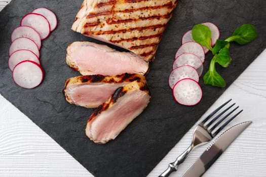 Sliced grilled pork fillet with fresh tomatoes and raddish served with glass of red wine.