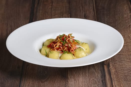 Plate with gnocchi, smoked bacon and cream sauce on wooden table.