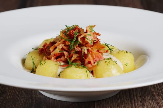 Plate with gnocchi, smoked bacon and cream sauce on wooden table.