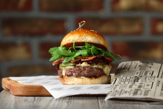 Burger on the wooden table with cheese, bacon, tomatos near newspaper.