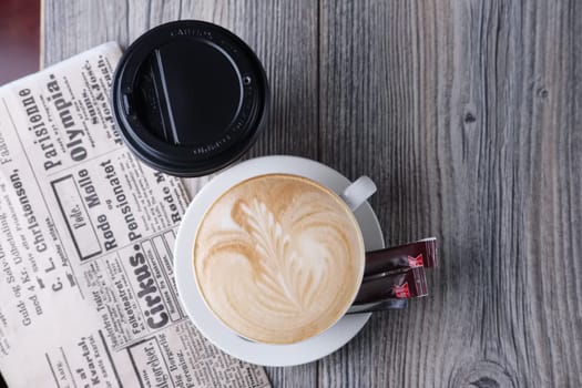 Ceramic and cardboard cup of coffee on wooden table near newspaper. Top view.