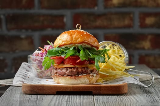 Burger on the wooden table with cheese, bacon, tomatos, green and red salad and french fries.