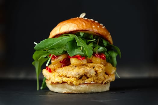 Close-up photo if chickenburger on black background with cheese, bacon, tomatos, green salad and chili.