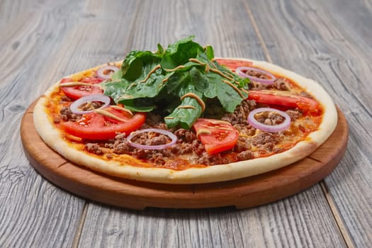 pizza with meat, spinach, tomato and red onion on wooden table