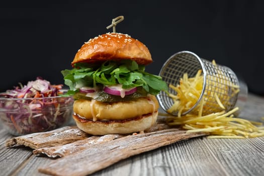 Fishburger on the wooden plates with cheese, cucumber, onion, green and red salad and french fries.