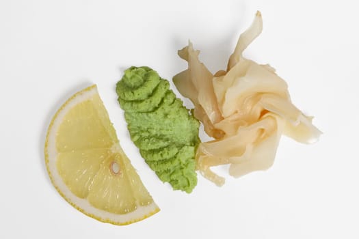 Top view of slice of lemon, wasabi and pickled ginger on white background with shadow.