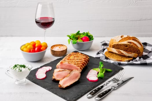 Sliced grilled pork fillet with fresh tomatoes and raddish served with glass of red wine.