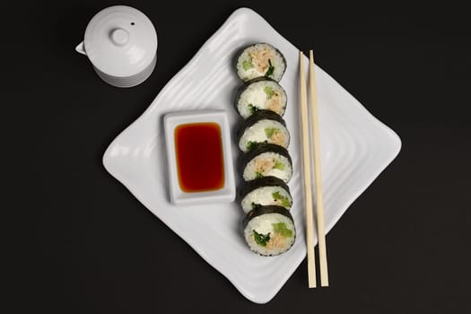 Top view of portion of chicken teriyaki rolls served on black paper with soy sauce and hashi.
