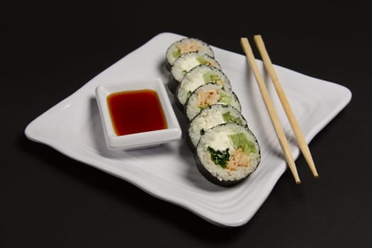 Angle view of portion of chicken teriyaki rolls served on black paper with soy sauce and hashi.
