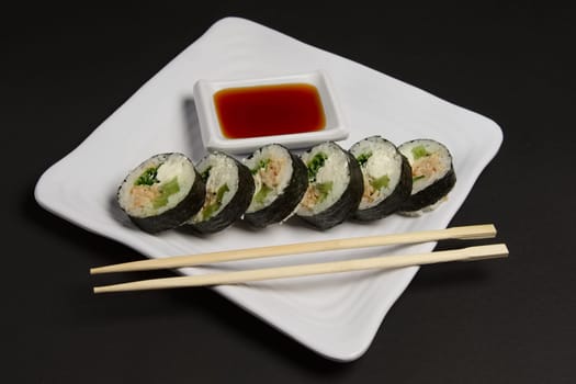 Angle view of portion of chicken teriyaki rolls served on black paper with soy sauce and hashi.