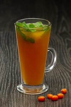 Glass of hot tea with sea buckthorn and mint on wooden table (soft focus photo