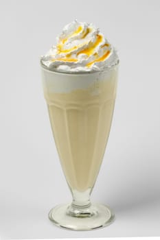 Mango and lemon milkshake summer cocktail in tall facetted glass on gray background
