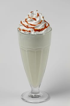 Melon and caramel milkshake summer cocktail in tall facetted glass on gray background