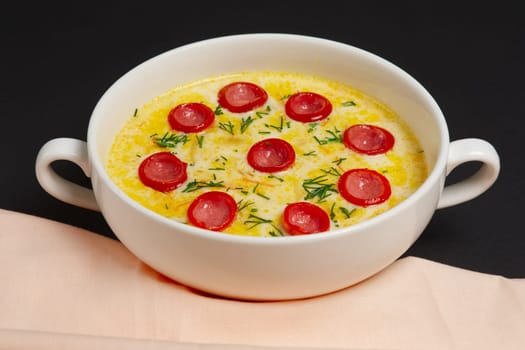 Bowl of pumpkin puree soup with smoked sausageon dark wooden table