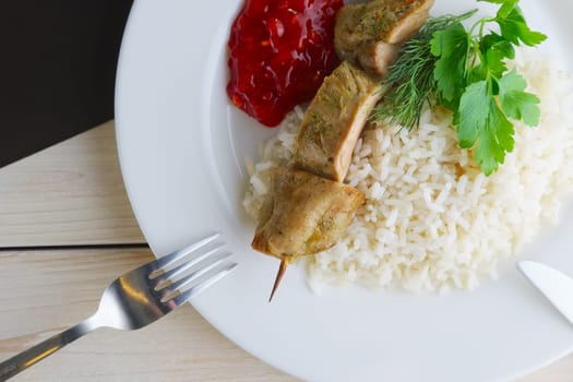 Close up view of plate with pork shaslyk with rice and tomato sauce on wooden table