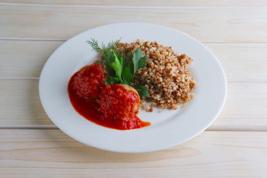 Traditional russian meatballs with buckwheat and tomato sauce on wooden table