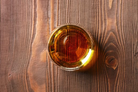 Top view of snifter glass with pure whiskey on dark wooden table