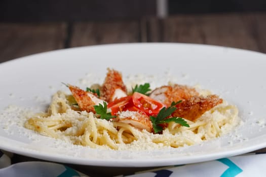 Close up view of spaghetti with chicken, tomato and cheese