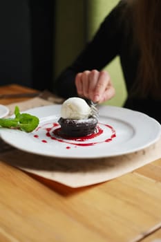 Shallow depth of foeld photo of brownie cake with ice-cream. Hand of girl with fork.