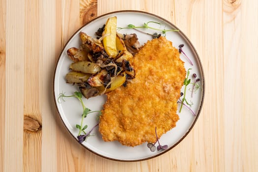 Tasty schnitzel in breading with fried potato, onion and mushrooms