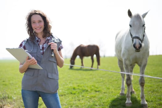 View of a young attractive veterinary in fields with horse