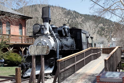 Idaho Springs, CO, USA - April 23, 2014: Front and side view of an old black train with historical information on a wood sign. A wooden walkway travels the length of the historical train to get a better closeup view.