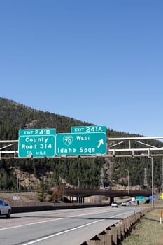 Idaho Springs, CO, USA - April 23, 2014: Two signs giving notice of exits in Idaho Springs with vehicles traveling on the highway during the day. Large green Interstate 70 exit signs in Clear Creek County on a bright blue sky day.