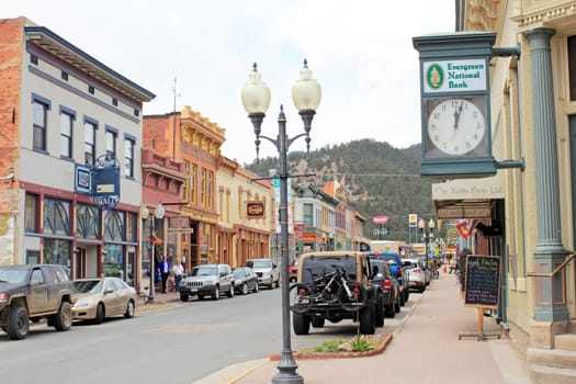 Idaho Springs, CO, USA - April 21, 2014: People shop in  historical buildings stores, restaurants and more enjoying the spring day on Miner Street in downtown. Many old and colorful buildings line both sides of the main street with many people and vehicles.