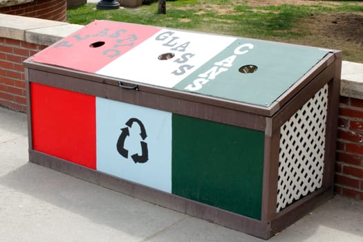 Idaho Springs, CO, USA - April 21, 2014: Hand painted wood bin in red, white and green to recycle plastic, glass and cans located on a sidewalk in front of Citizens Park on Miner Street.  A recycle bin center for plastic, glass and cans on a sidewalk in front of a a low brick wall during the day.