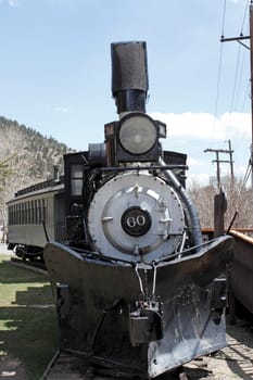 Idaho Springs, CO, USA - April 23, 2014: A black antique railroad train on a track at a public museum outdoors on a sunny day. The front of a vintage train engine and caboose behind it on a railroad track outside.