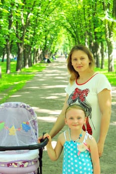 woman with baby in perambulator and elder daughter in the park