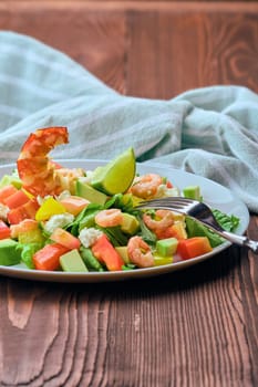 Salad with avocado, feta cheese and shrimps on old wooden table