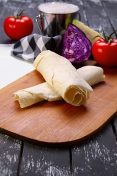 Rolled pita with fresh vegetables on wooden board with a napkin on a table.
