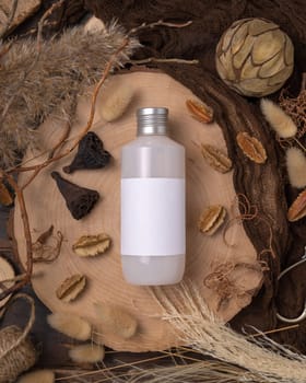 Bottle blank label on wood near natural boho decorations top view, cosmetic package mockup. Eco friendly skincare product, lotion or cream. Bohemian flat lay with dried leaves and flowers.