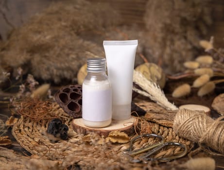 Cream bottle and tube on wood near natural boho decorations close up, cosmetics label mockup. Eco friendly Skincare beauty product, lotion or balsam. Bohemian composition with dried leaves and flowers.