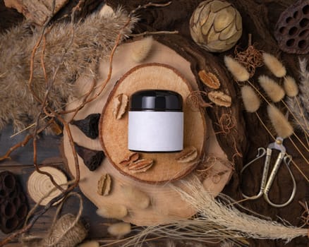 Cream jar with blank label on wood near natural boho decorations top view, cosmetic packaging mockup. Skincare product for everyday beauty routine. Bohemian eco friendly flat lay with dried leaves.