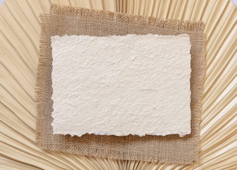 Blank handmade paper card on dry beige palm leaf near hare's tail grass top view, mockup. Boho scene with horizontal card. Bohemian or close to nature greeting card or wedding Invitation.