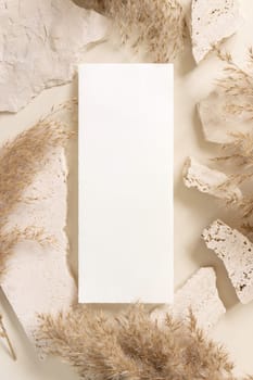 Blank card near beige travertine stones and dried pampas grass top view, mockup. Boho scene with vertical card. Bohemian or close to nature greeting or wedding Invitation. Close to nature.