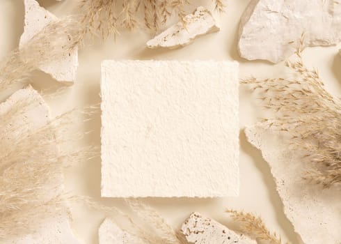 Square card near beige travertine stones and dried pampas grass top view, mockup. Boho scene with handmade paper card. Bohemian or close to nature greeting or wedding Invitation. Close to nature.