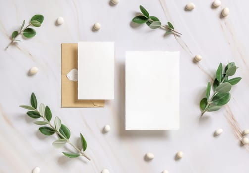Cards and envelope on a marble table near eucalyptus branches and pebbles top view, Mockup. Romantic flat lay with wedding stationery set. Minimal composition. Close to nature